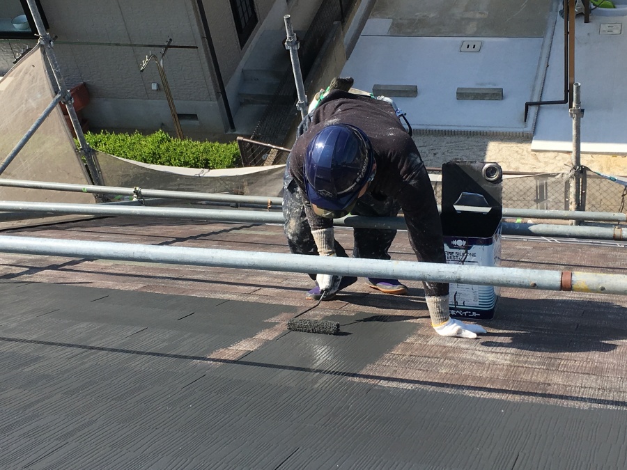 スレート屋根に足場を組んで塗料をローラーで塗布していく職人