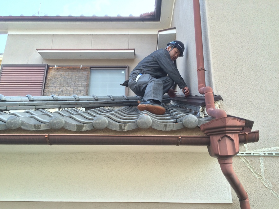 職人が屋根に上り瓦屋根と漆喰などの現地調査